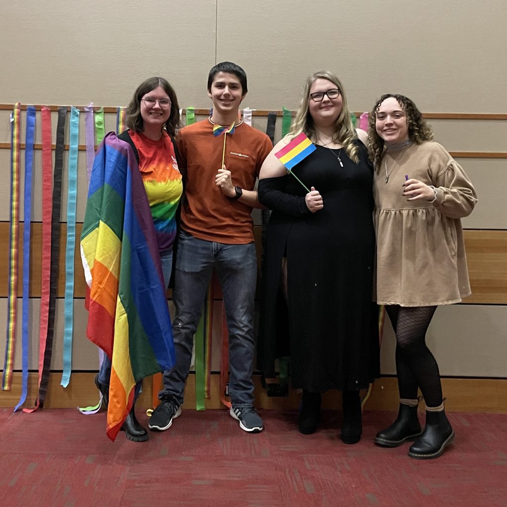 Sarah Rasing, M.Ed., poses for a photo with three Valpo students, each smiling as they hold up various pride flags.
