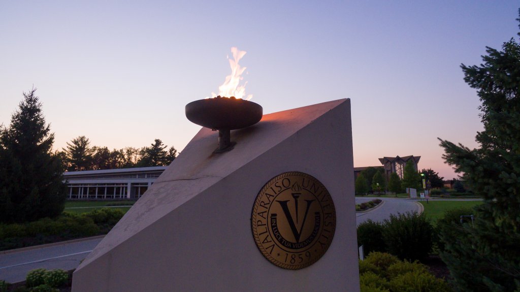 stone entrance sign with university seal and lit torch