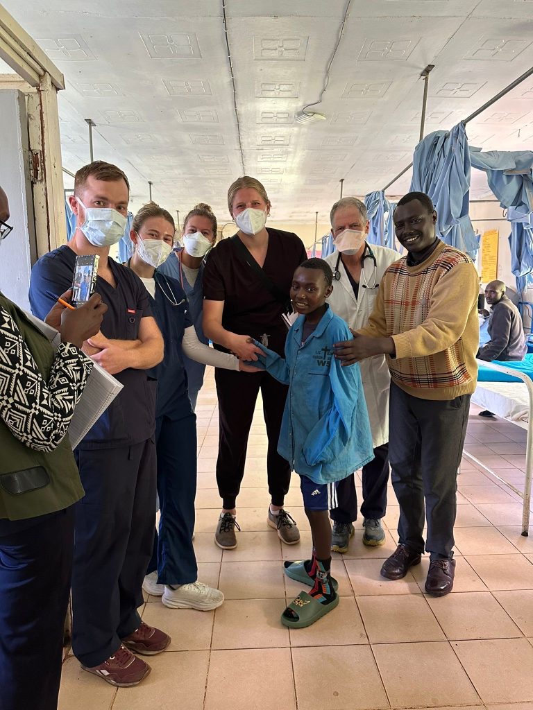 Valparaiso University alumna Cailey Rooker '24 dressed in medical scrubs and mask, standing alongside members of her medical team and two patients.