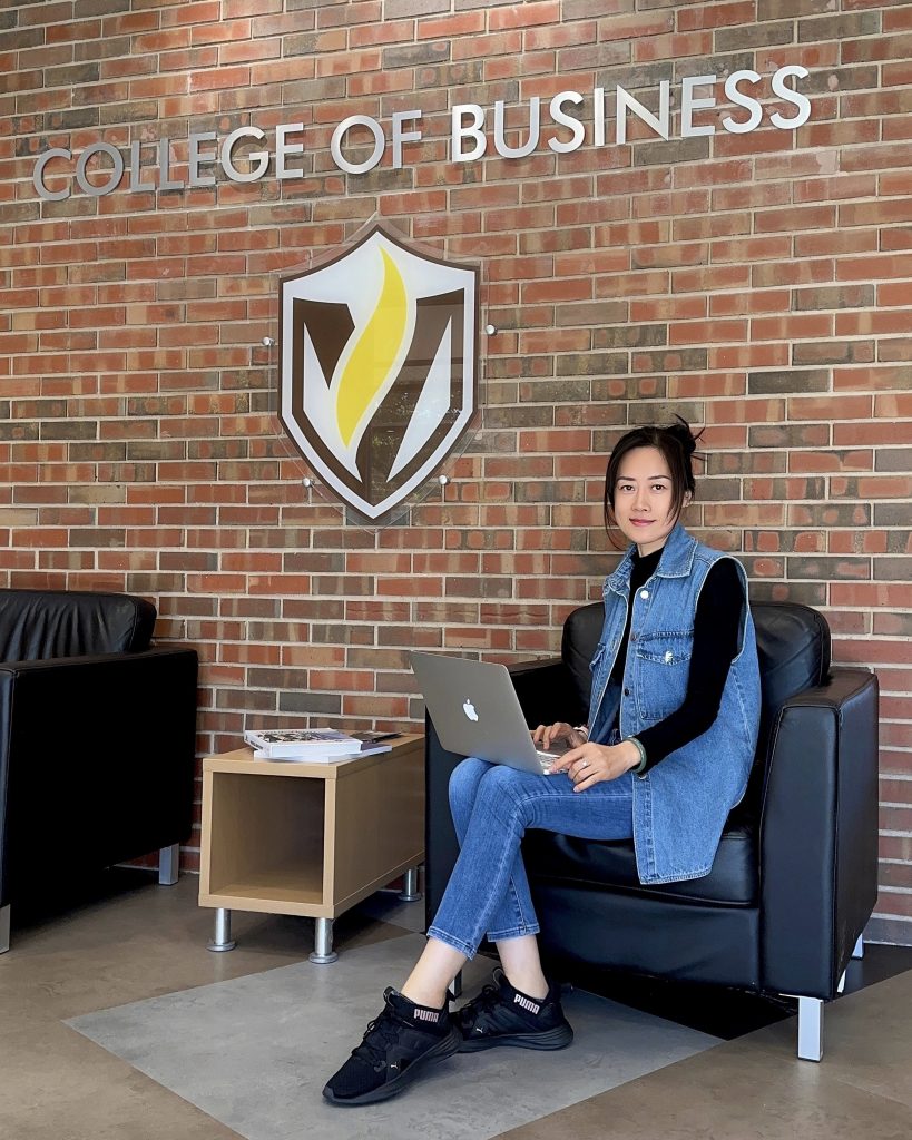 Valparaiso University business student Yingxin (Grace) Zhang ’25 sits with her laptop on her lap in the lobby of Valpo's College of Business.