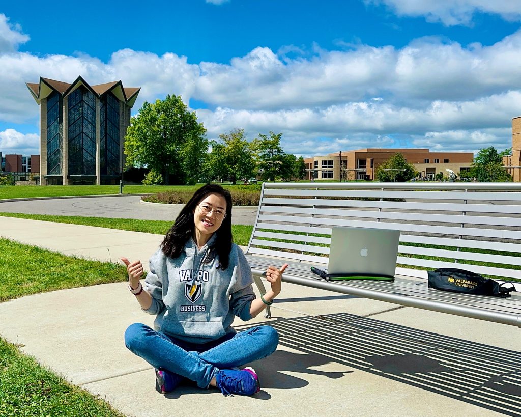 Yingxin (Grace) Zhang ’25 sits smiling with thumbs up in front of the Chapel of the Resurrection.