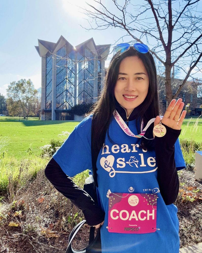 Valparaiso University business student Yingxin (Grace) Zhang ’25 stands in front of the Chapel of the Resurrection, smiling while holding up a medal.