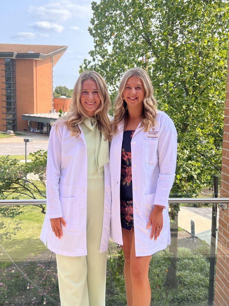 Valparaiso University alumni Cailey Rooker '24 and Rachel Yeager '24 posing for a photo, smiling and wearing medical white coats.