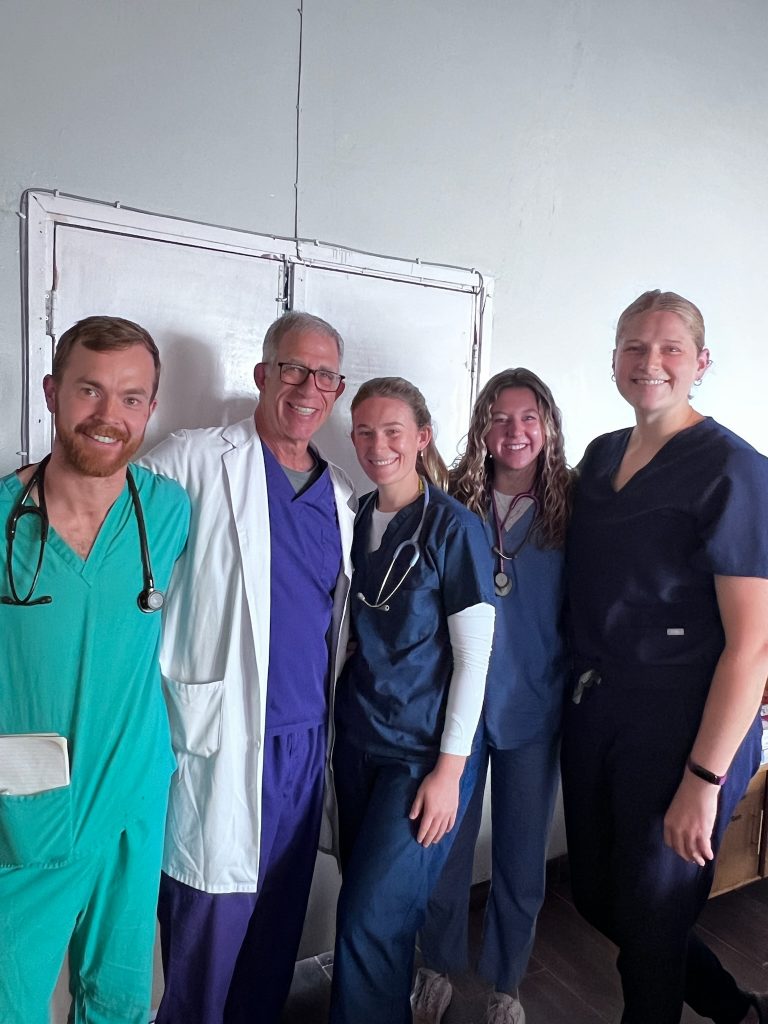 Valparaiso University alumna Cailey Rooker '24 dressed in medical scrubs, standing alongside members of her medical team all smiling and posing for a photo.