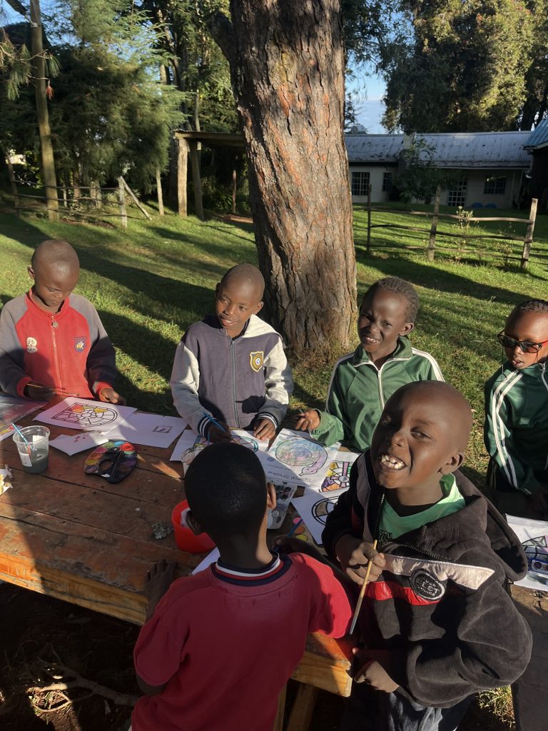 Several young Kenyan children sitting around a picnic table outside, smiling and posing for the camera.