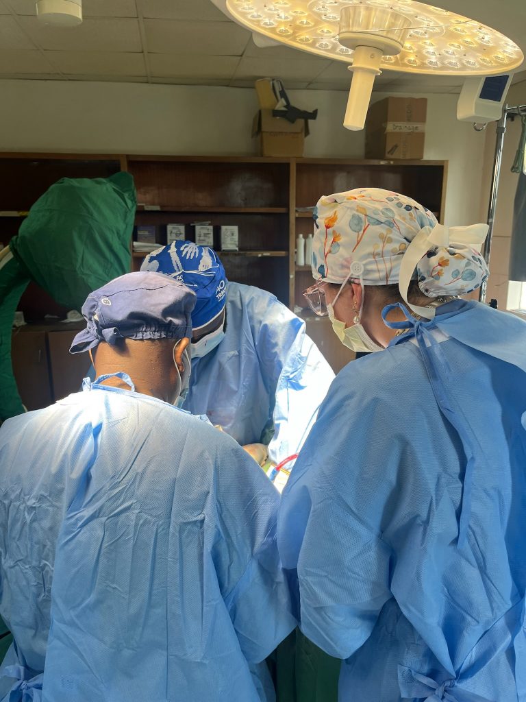 Valparaiso University alumna Cailey Rooker '24 dressed in medical scrubs and a mask, facing an operating table and assisting with surgery.