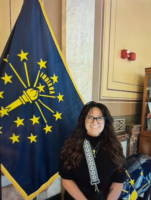 Valparaiso University social work student Rhonda Collier '25 smiles in front of Indiana's state flag.