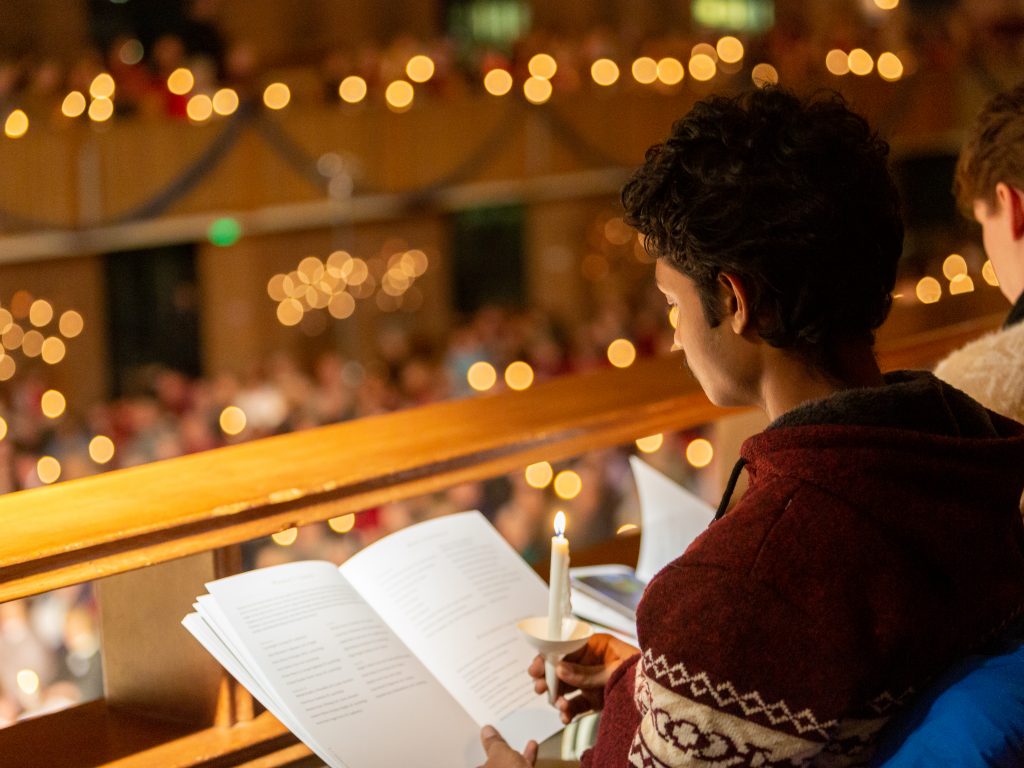 A student holds a program and a candle in the pews of the Chapel during a candlelit event.