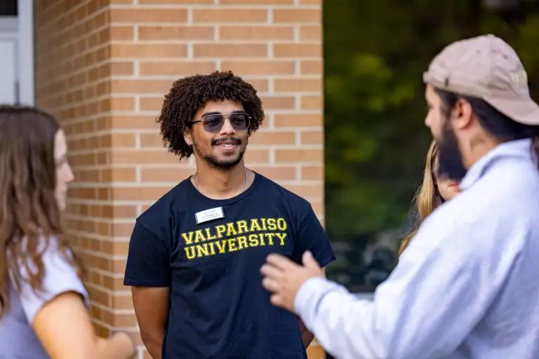 Fox Wilmot '24 wears a black t-shirt with VALPARAISO UNIVERSITY on it while he smiles with his fellow students.